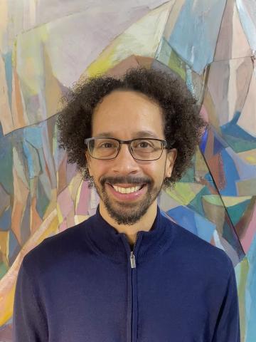 poet wearing a blue shirt with an abstract painting in the background