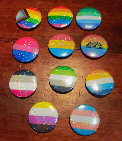 Variety of pride flag buttons on a wooden surface