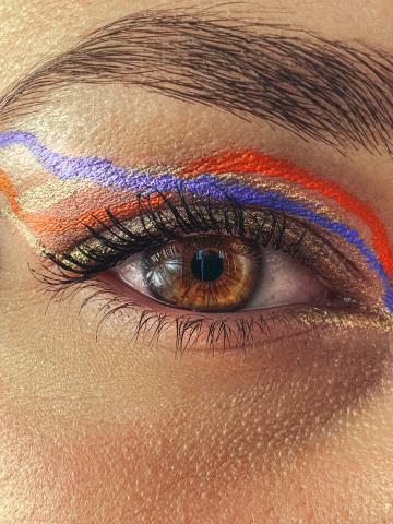 close up photo of an eye with red, blue, and yellow eyeliner along the brow bone