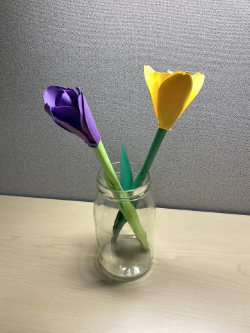 Two paper tulips in a glass jar. One tulip has a purple bulb and the other a yellow bulb.
