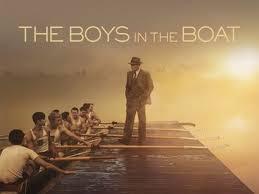 The Boys in the Boat - a dock with the rowers on one one side and man on the dock in morning sun