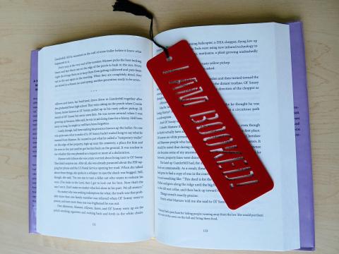 A red laser cut bookmark sits on top of a book. It has stencil-style letters reading "I am booked"