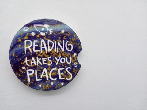 Coaster with a galaxy background says "reading takes you places"