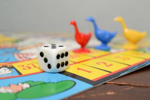 This image depicts a game board with three different colored geese figurines and a six-sided die. 