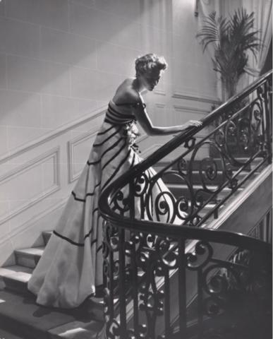 A black and white photo of a woman ascending a staircase, wearing a formal gown.