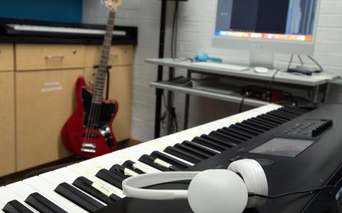 An electronic keyboard and bass are staged alongside an Apple Mac computer with Garageband open on the screen.