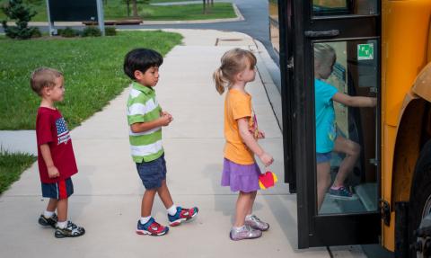 Four kindergarten-aged students boarding a yellow school bus.