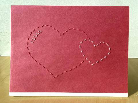 a card of red craftpaper over white cardstock sewn with thread in the outline of two hearts 