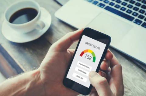 Hands holding a phone checking a credit score. In the background are a cup of coffee and a laptop keyboard. 