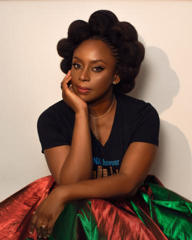 on a pale pink background, adichie is wearing a black top and a red and green skirt