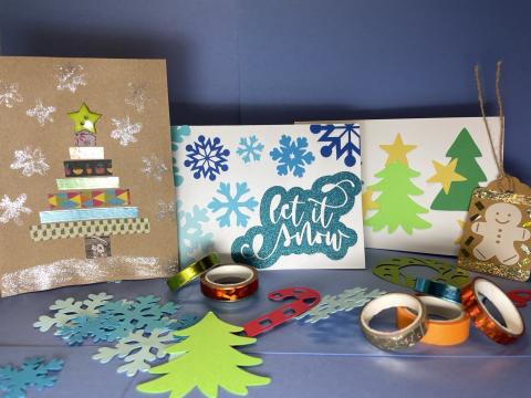 Three holiday cards and a gift tag among holiday and winter themed paper cut-outs and colorful washi tape. 