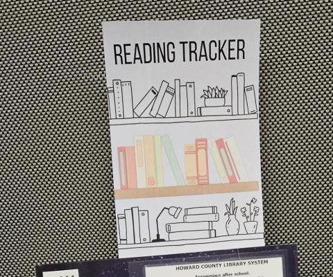 a bookmark in a book, the bookmark says "reading tracker" at the top and then has images of a shelf of books with blank spines to track ones reading