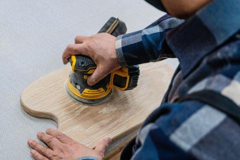 piece of wood being sanded by a person in a blue shirt with their back to the camera