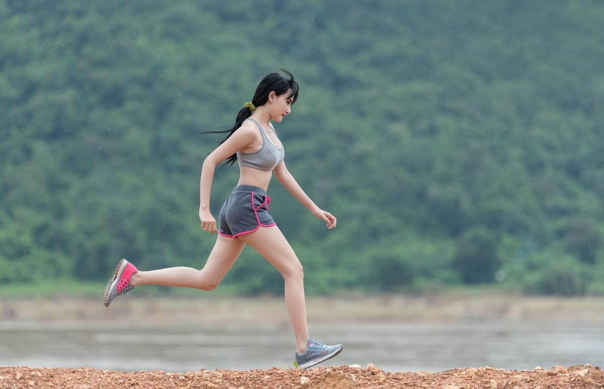 Woman in shorts running out doors on a flat trail.