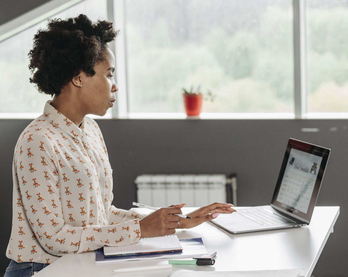 Woman using a laptop computer at a desk in front of a window.