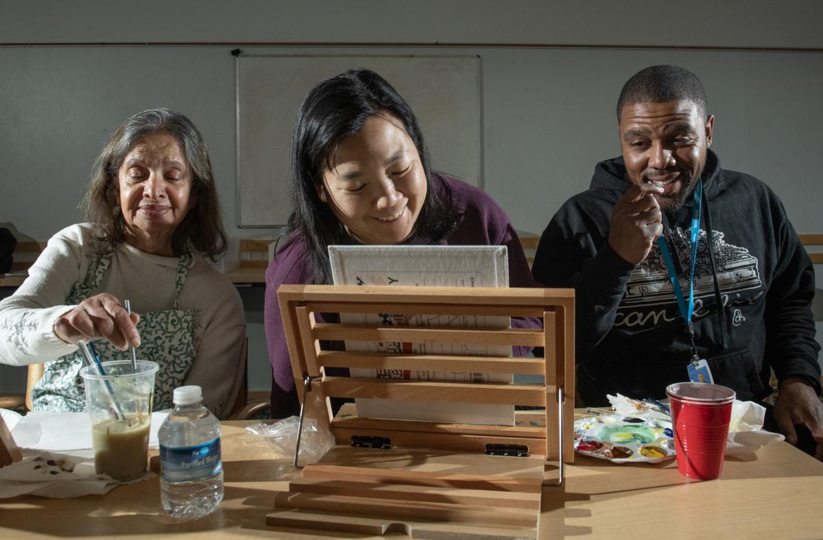 three adults creating art pieces together at a table