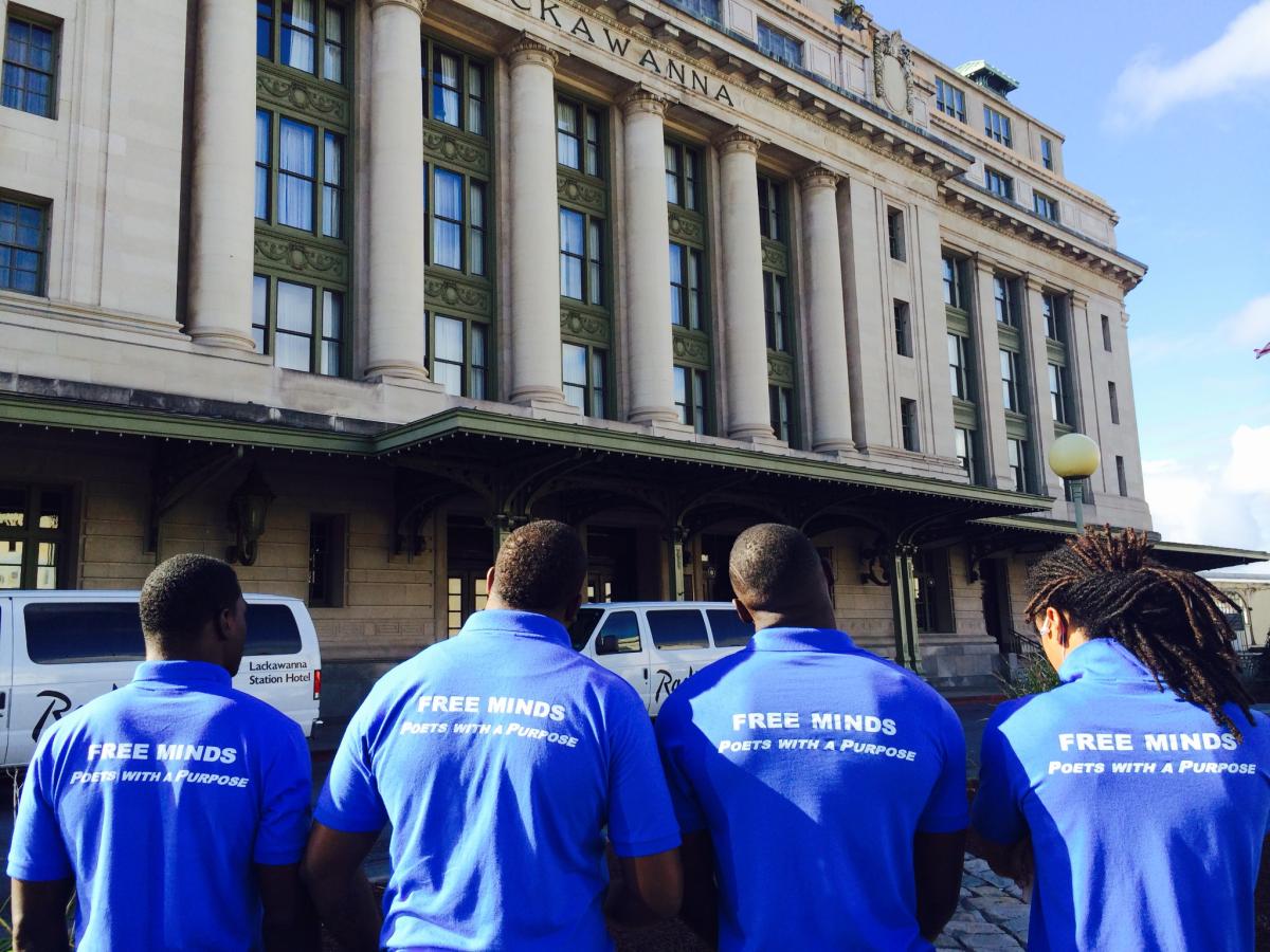 four young people showing their back and wearing a blue shirt with poetry with a purpose written on it 