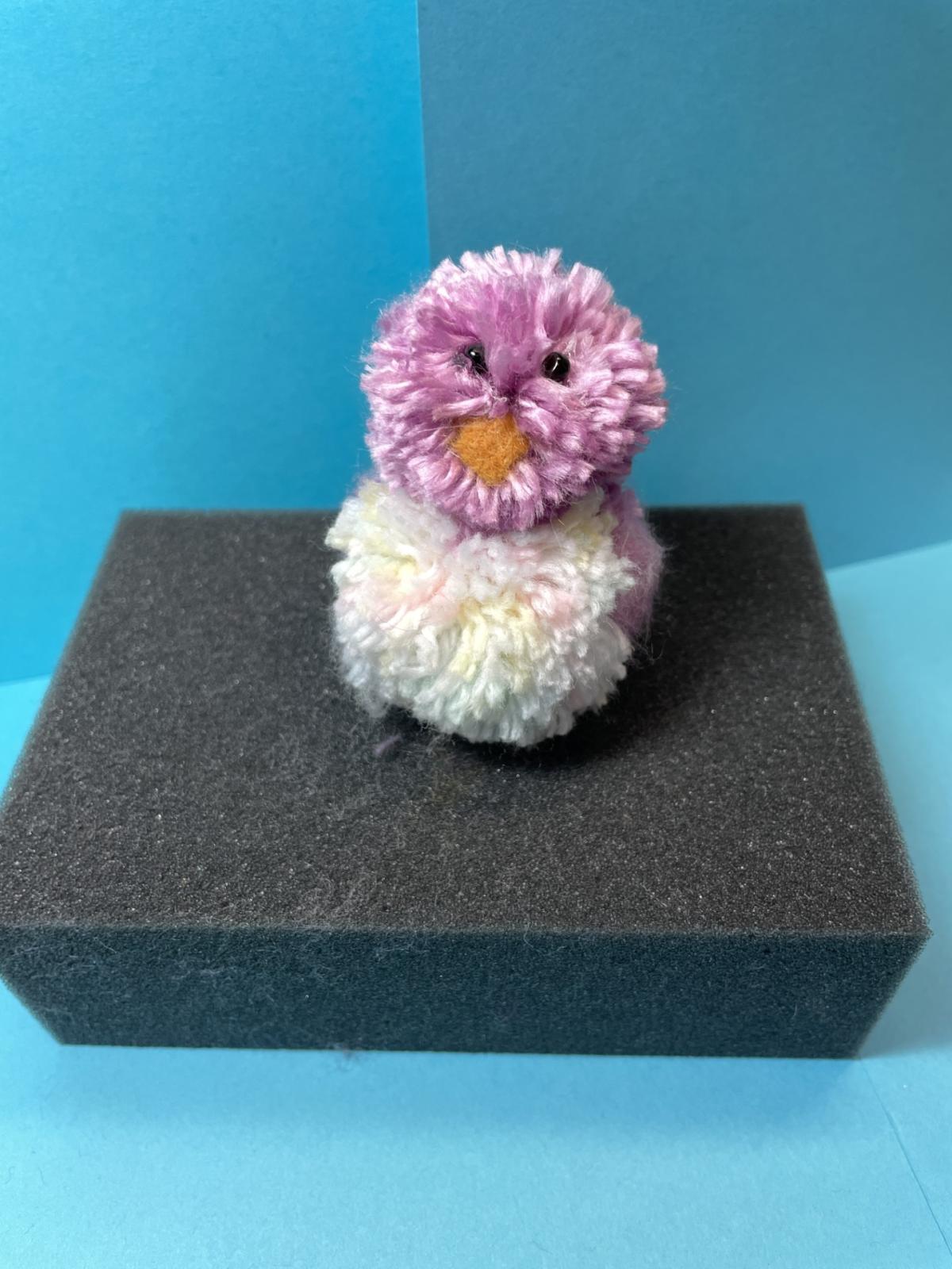 a purple bird made out of yarn pom poms with a light-colored tummy.