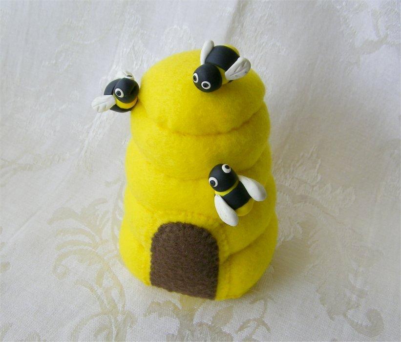 photo of a pincushion handmade out of yellow felt to look like an old fashioned beehive, 3 pins are stuck in it which have clay honeybees on the ends