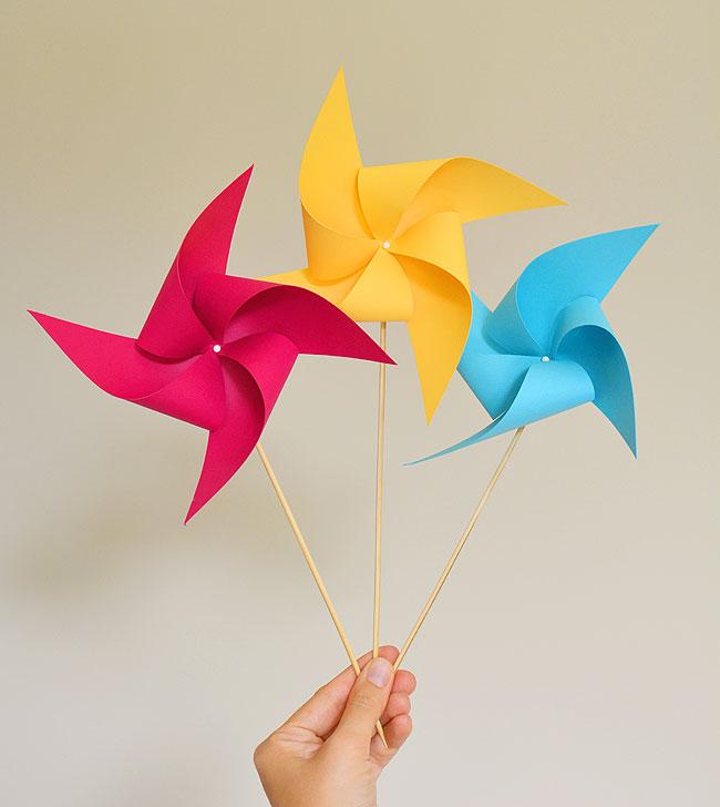 Hand holding pink, yellow, and blue paper pinwheels.