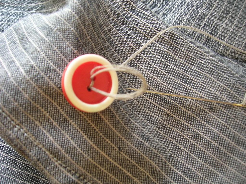 Red & white button in process of sewing on - Flikr Creative Commons