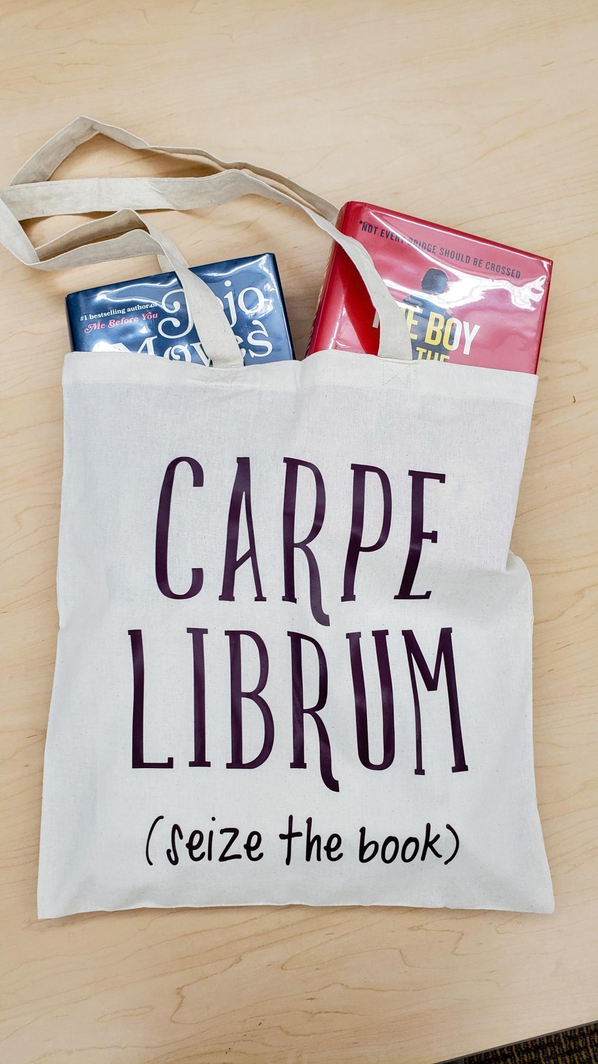 Canvas book tote with the text "Carpe Librum (seize the books)" is pictured with books spilling out of the top