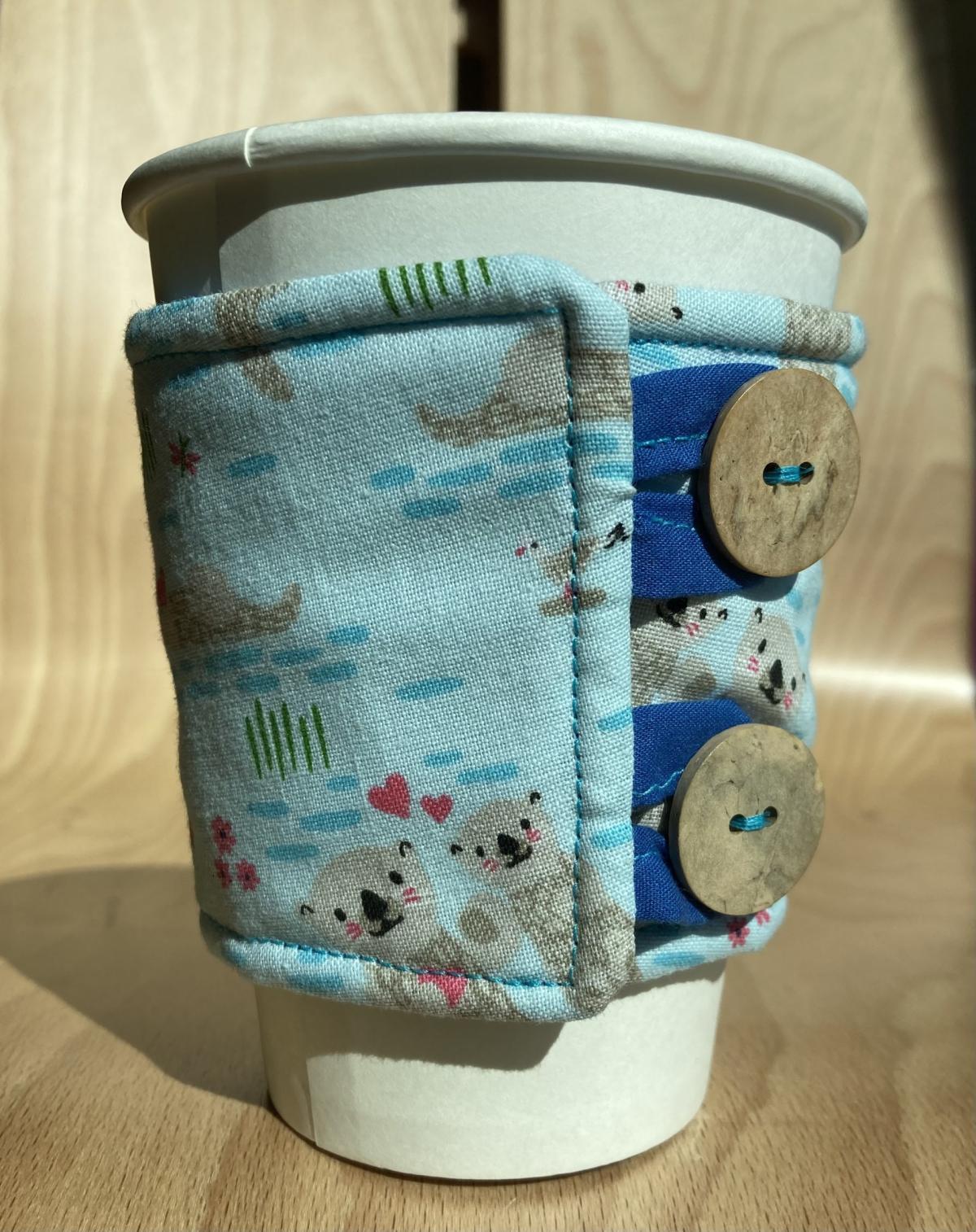 blue fabric coffee cozy with tan buttons on a white paper cup