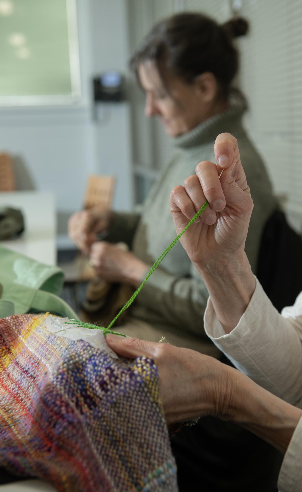 Close up photo of hand sewing with a needle and green thread