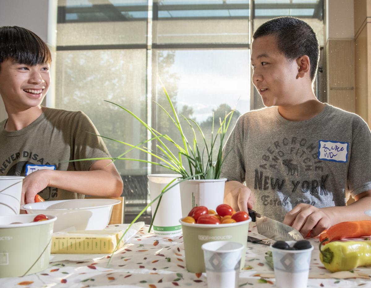 Two teens chopping herbs and tomatoes in a culinary class.
