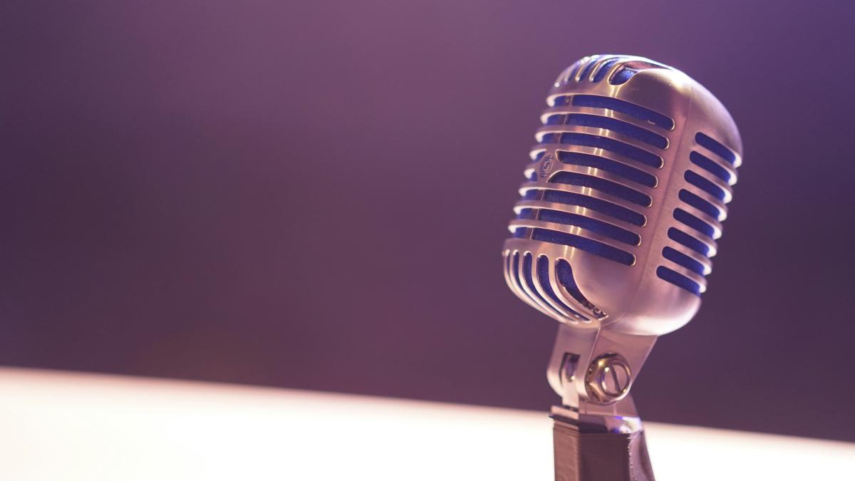 A closeup photo of a microphone onstage with a spotlight being shined on it.