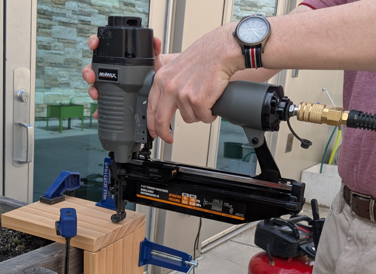 Close-up of hands holding a pneumatic nailer against wood