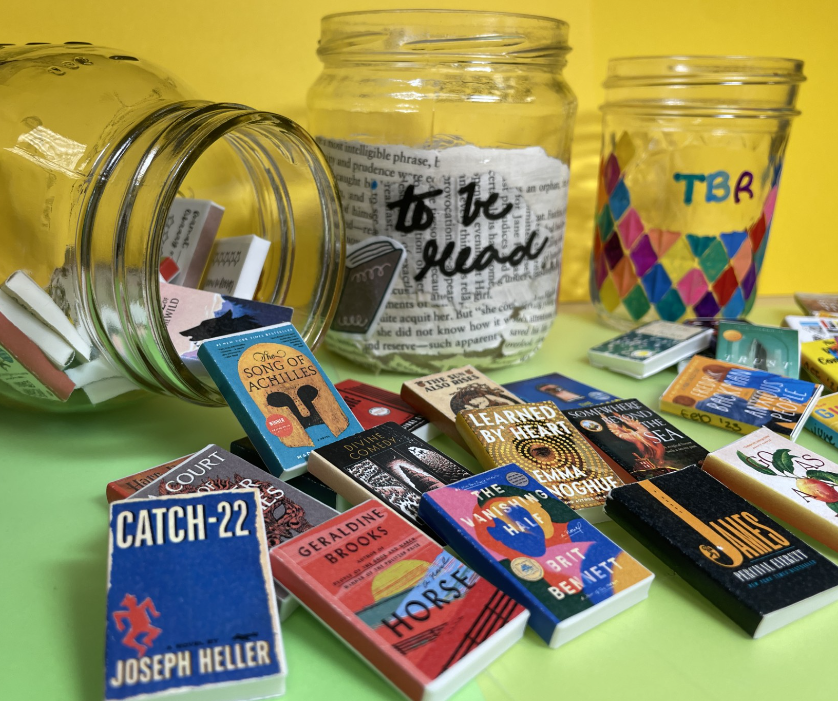 three glass jars decorated with book pages and paint pens; miniature books in the foreground. 