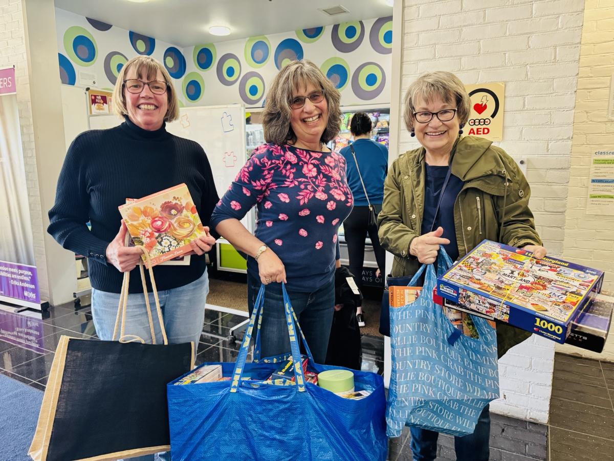 Three people pose for a photo, holding some of the puzzles they found at the swap!