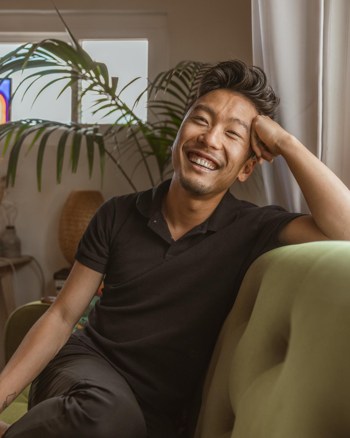 Headshot of author Scott Shigeoka on couch  smiling with hand against forehead