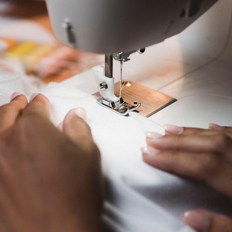 A close-up of hands guiding fabric through a sewing machine (Freepik)