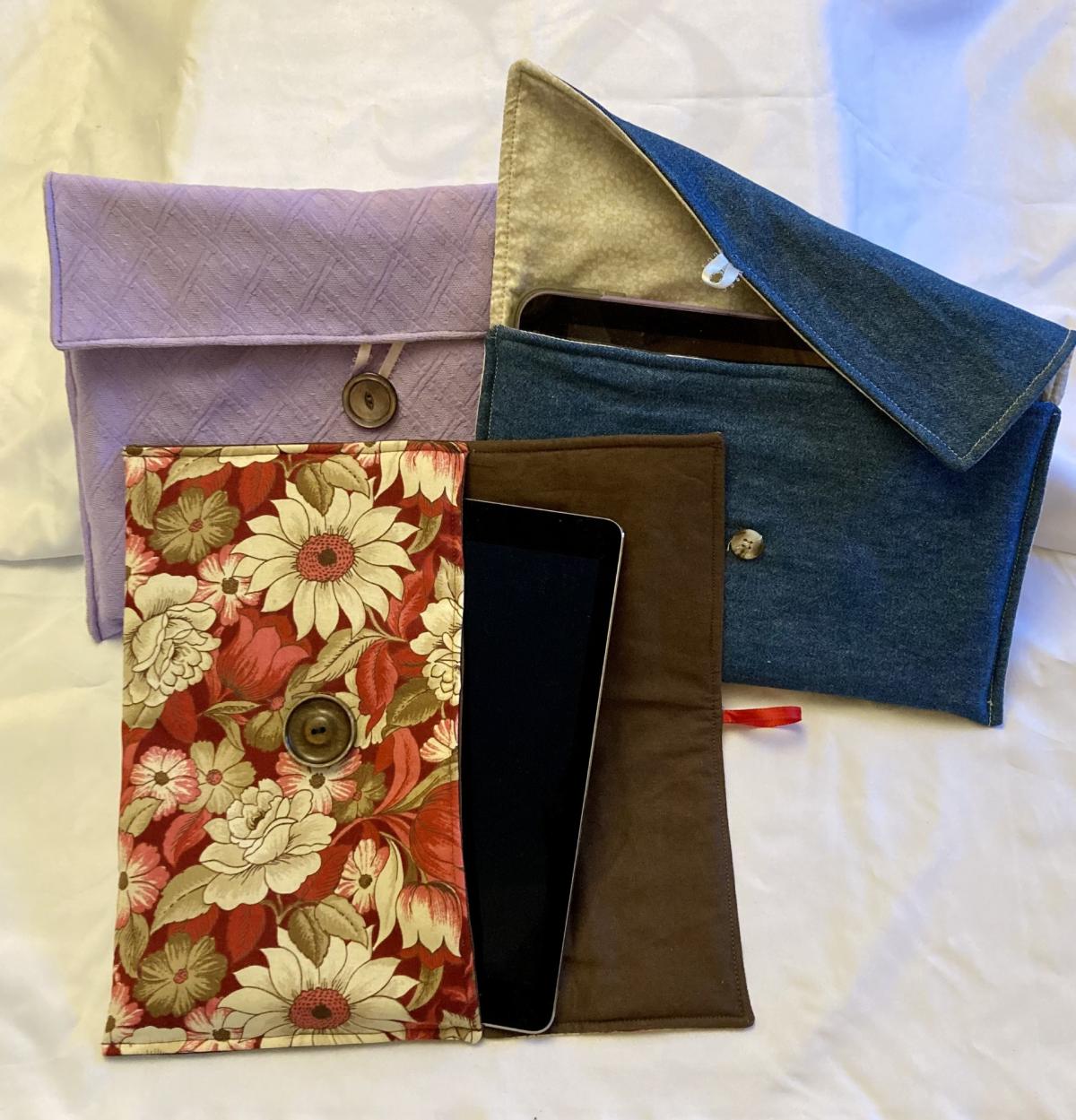 Three fabric pouches of different colors holding electronic tablets against a white background
